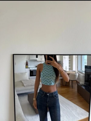 Grönmönstrad croppad linnetopp - Snygg croppad linnetopp med grönt och vitt retroinspirerat mönster. Toppen är ärmlös med hög hals och sitter tight mot kroppen. Perfekt för dig som vill sticka ut med en färgglad och trendig look.