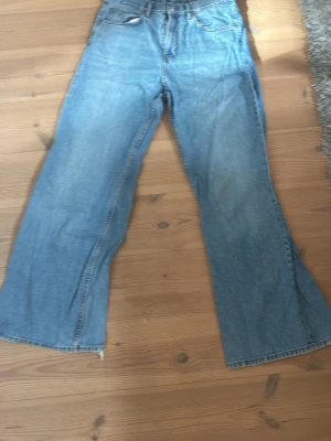 Blåa utsvängda jeans - Ett par ljusblå jeans med utsvängda ben och klassisk femficksdesign. Jeansen har hög midja och är tillverkade i denim. Perfekta för en avslappnad och trendig stil.