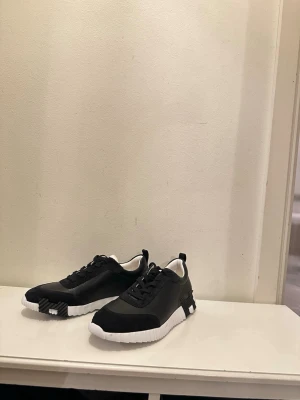 Svarta sneakers med vit sula - Stilrena svarta sneakers med chunky vit sula och svarta skosnören. Ovandelen är i en mix av textil och mockaliknande material. Snygg kontrast mellan svart och vitt, perfekt för en modern streetstyle-look.