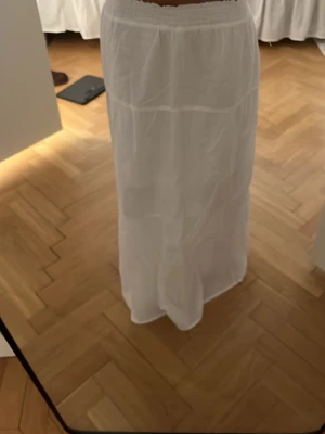 Vit långkjol med resårmidja - Säljer en enkel och luftig vit långkjol med resår i midjan. Kjolen har en flowy passform och är tillverkad i ett tunt, lätt material som passar perfekt till varmare dagar. Stilren design utan mönster eller extra detaljer.