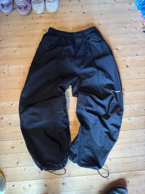 Baggy skidbyxor från Beyond Medals - Svarta baggy skidbyxor från Beyond Medals med avslappnad passform och justerbara benslut med dragsko. Perfekta för kalla dagar och vinteraktiviteter. Elastisk midja för extra komfort och stilren logga på benet.