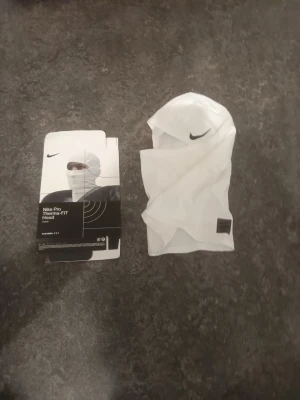 Nike Pro Therma-FIT Hood vit - Nike Pro Therma-FIT Hood i vitt, tillverkad i ett mjukt och isolerande material som håller dig varm. Snygg och sportig design med Nike-logga på sidan. Perfekt för träning eller utomhusaktiviteter när det är kallt.