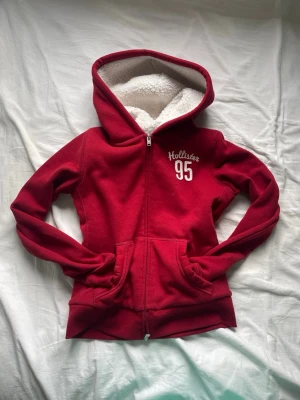 Röd Hollister hoodie med dragkedja - Köpte denna i vintras men har bara andvända den en gång. Den är jättemysig och varm, perfekt till hösten och vintern. Den är en figurnära hoodie. Så den passar allt ifrån XXS-S. 