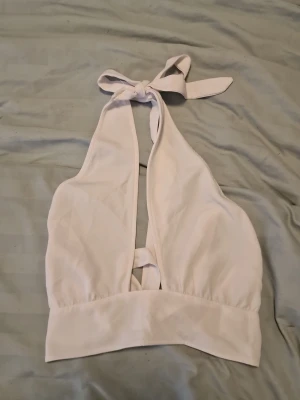 Vit linnetopp med knyt i nacken - Snygg vit linnetopp med knyt både i nacken och bak. Toppen är ärmlös och har en djup urringning framtill. Perfekt för varma dagar och enkel att styla till olika outfits. Tillverkad i mjukt bomullsmaterial för en bekväm känsla.