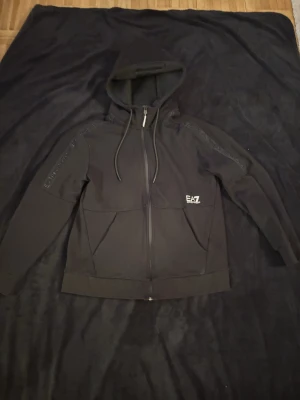 Ea7 zip up  - Svart EA7 Hoodie i storlek M. Passar perfekt till dig som vill är en enkel och simpel person. Perfekt för en chill dag. Mitt pris 449