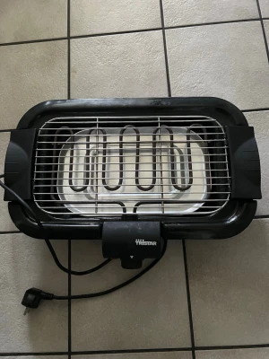 Svart elektrisk bordsgrill Tristar - Elektrisk bordsgrill från Tristar i svart plast och metall. Rektangulär form med metallgaller och synlig värmeslinga. Perfekt för att grilla inomhus, enkel att använda med sladd och stickkontakt.