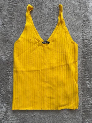 Gul ribbad linnetopp från Gina Tricot - Snygg gul ribbad linnetopp från Gina Tricot med v-ringning och smala axelband. Perfekt för dig som vill ha en färgglad och bekväm topp till sommaren. Tillverkad i mjuk bomull med stretch för extra komfort.