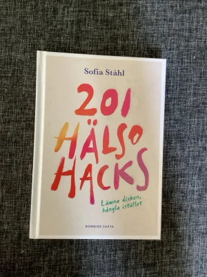 201 Hälsohacks av Sofia Ståhl - En inspirerande bok med titeln '201 Hälsohacks' av Sofia Ståhl. Omslaget är vitt med färgglad text i rosa, orange och lila. Boken är inbunden och ger tips för bättre välmående och balans i livet.
