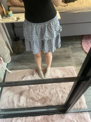 Blommig blå volangkjol  - Supersöt blå kortkjol från Vila med vitt blommönster och volangdetaljer. Lätt och luftig känsla parfekt till sommar och våren💗