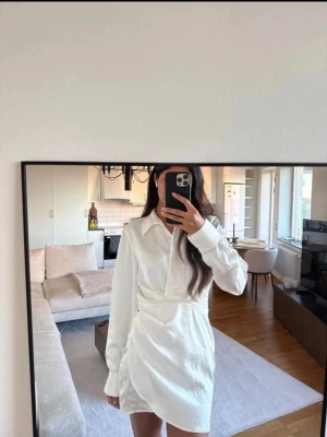 Vit omlottklänning med krage från Zara - Snygg vit kort omlottklänning med skjortkrage och långa ärmar. Klänningen har en markerad midja. Perfekt för dig som gillar en clean och trendig look. Passar nu inför student, examen eller fester. Nypris 399kr