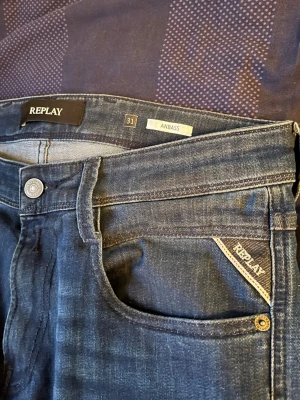Blå jeans Replay Anbass herr - Säljer ett par snygga blå jeans från Replay, modell Anbass. Klassisk femficksdesign med Replay-logga på fickan och patch bak i midjan. Jeansen har en smal passform och är tillverkade i stretchigt denimtyg för extra komfort.
