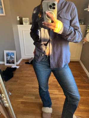Blå skjorta med ficka och knappar - Snygg blå skjorta med klassisk krage och bröstficka. Skjortan har långa ärmar och stängs med knappar framtill. Perfekt för en avslappnad men ändå stilren look.