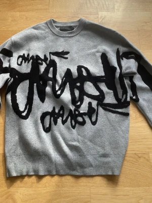 Grå stickad tröja med svart print - Snygg grå stickad tröja från Zara med unikt svart grafiskt mönster framtill. Tröjan har rund halsringning, långa ärmar och ribbade muddar. 