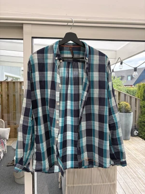Nudie jeans skjorta - Snygg rutig skjorta från nudie i blå, turkos och vit. Skjortan har klassisk krage, knäppning framtill och långa ärmar. Perfekt för en avslappnad och trendig look.
