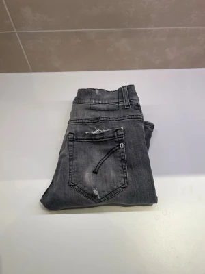 Grå slitna jeans med hål - Snygga grå jeans med slitningar och hål på benen för en trendig och avslappnad look. Jeansen har klassisk femficksdesign och normal midja. Perfekta för dig som gillar streetstyle och vill ha en cool vibe i vardagen. Har en fläck på höger knä men går bort i tvätten