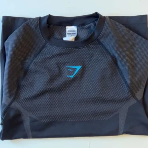 Gymshark onyx v5 long sleeve tshirt - Svart långärmad seamless träningströja från Gymshark med blå logga. Storlek M. Slutsåld online. Säljer då den inte används. Endast använd ett fåtal gånger. Priset kan diskuteras