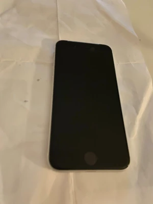 Vit iPhone med Touch ID iPhone SE - Säljer en stilren vit iPhone med rund hemknapp och Touch ID. Baksidan är i glas med en enkel kamera och Apple-logga i mitten. Telefonen har rundade kanter och klassisk Apple-design. Perfekt för dig som gillar snygg och enkel mobil.