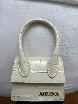 Vit  Le Chiquito handväska - Säljer en superfin vit  Le Chiquito handväska i croc-embossat läder. Väskan har ett topphandtag och guldfärgad -logga framtill. Perfekt statement piece för dig som gillar trendiga accessoarer.