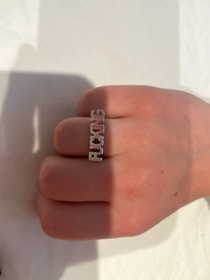 Silverring med text: ”Fucking” - Cool silverfärgad ring med texten 'FUCKING' i stora bokstäver. Ringen är från Lotta Hasselblad och är två år gammal och hyfsat använd. 