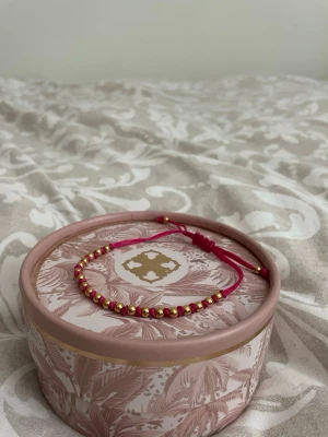 Rosa armband med guldpärlor - Snyggt armband med rosa snöre och små guldfärgade pärlor. Justerbar knut för perfekt passform. 