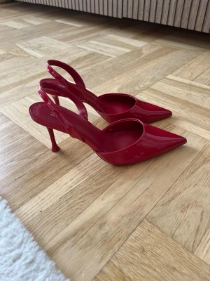 Röda lackpumps med spetsig tå - Snygga röda pumps i lack med spetsig tå och smal klack. Skorna har en öppen häl med slingback-rem och en elegant, modern design som verkligen sticker ut. 