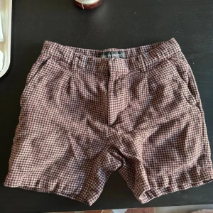 Rutiga shorts från Wacko Maria - Rutiga shorts i vinröd från japanska streetwear märket Wacko Maria. Klassisk passform med resår i midjan, sidofickor och bakfickor med knapp