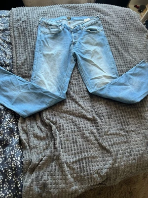 Ljusblå jeans från Lee - Säljer ett par ljusblå jeans från Jack & Jones med klassisk femficksdesign och raka ben. Storleken W32 L32. Jeansen har snygga slitningar och är tillverkade i bomull med lite stretch för extra komfort. Perfekt för dig som gillar en avslappnad och trendig look.