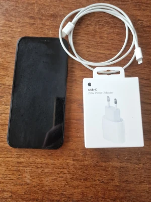 Svart iPhone 12 med ny laddare och sladd - Säljer en svart iPhone 12 från Apple. Telefonen har en stilren design med glasbaksida, dubbla kameror och rundade hörn. Medföljer gör en vit USB-C laddare (20W) och en vit laddningskabel. Perfekt för dig som vill ha en snygg och snabb mobil. Helt ny strömadapter, skärmskydd sitter på redan. Rengjord. F. D företagsmoil. 