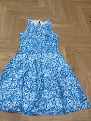 Blåvit mönstrad klänning från FB Sister - Säljer en blåvit ärmlös klänning från FB Sister med ett detaljerat paisleymönster. Klänningen har en rund halsringning och en liten öppning bak i nacken. Passformen är normal och tyget känns mjukt och bekvämt, perfekt för varma dagar.