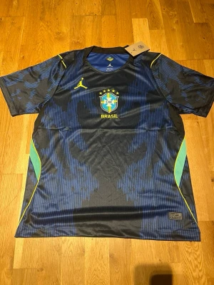 Brasilien matchtröja blå Nike - Snygg blå och svart Brasilien matchtröja från Nike med gula detaljer och CBF-logga på bröstet. Tröjan har korta ärmar, rund hals och gröna inslag på sidorna. Tillverkad i lätt och ventilerande material, perfekt för fotboll eller träning.