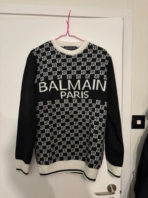 Svartvit stickad tröja Balmain Paris - Säljer en svartvit stickad tröja från Balmain Paris med grafiskt mönster och stor logotyp på bröstet. Tröjan har rund halsringning, långa ärmar och ribbade muddar i vitt. Perfekt för dig som gillar exklusiva märken och trendig design. Tröjan är såklart äkta men kommer knappt till användning. Endast seriösa köpare!