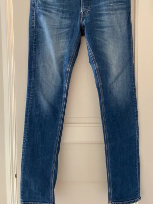 Replay Jeans  - Säljer ett par blå Replay jeans med snygga slitningar och kontrastsömmar. Jeansen har klassiska femficksdetaljer och ljusare partier på låren. Perfekt för dig som gillar en avslappnad och trendig look.