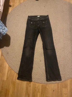 Svarta bootcut jeans med fickor - Säljer ett par svarta bootcut jeans med snygga detaljer på framfickorna och kontrastsömmar. Jeansen har klassisk femficksdesign och är tillverkade i ett mjukt denimtyg. Perfekta för dig som gillar en tidlös och cool stil.