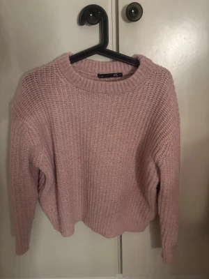 Rosa stickad tröja från lager  157 - Mysig rosa stickad tröja från Lager  157 med rund halsringning och grovstickad struktur. Tröjan har långa ärmar och ribbade muddar vid hals, ärmslut och nederkant. Perfekt för kalla dagar.