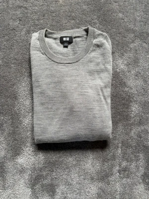 Ljusgrå tunn tröja från Uniqlo - Säljer en stilren ljusgrå tröja från Uniqlo. Tröjan är tunnstickad med rund halsringning och långa ärmar. Perfekt för lager på lager och enkel att matcha med olika outfits. Materialet känns mjukt och lätt mot huden.