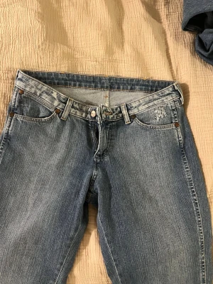 Blå Wrangler jeans med klassisk passform - Säljer ett par blå low waist jeans från Wrangler med snygga kontrastsömmar och broderad logga, mkt fint skick. Köpta på Vinted i veckan, säljer pga för korta på mig som är 177 cm (brukar ha L32-34). Passar nog perfekt för ngn som är under 170! Brukar ha W: 28 men dessa passade ändå jättebra. Snygg klassisk denim wash. 