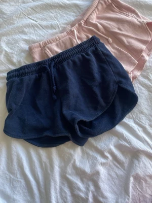 Mörkblå och rosa  shorts från Primark XS - Säljer två  par shorts från Primark i mjuk frotté med elastisk midja och snörning. Perfekta för sommardagar eller att chilla i hemma. Klassisk sportig look och riktigt sköna att bära.