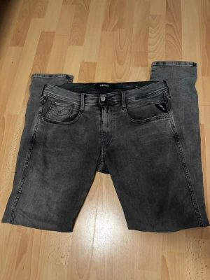 Grå jeans från Replay - Storlek W33 L32 .Säljer ett par snygga grå jeans från Replay med klassisk femficksmodell och svarta detaljer. Jeansen har en tvättad look och raka ben. Materialet är mjukt denim som sitter skönt och passar till det mesta. Perfekt för dig som gillar stilrena och trendiga jeans.