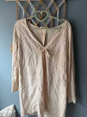 Ljusbeige långärmad klänning - Söt ljusbeige klänning med v-ringning och lång ärm. Klänningen har fina spetsdetaljer och en liten rosett framtill. Tillverkad i ett mjukt material som känns skönt mot huden. Perfekt för dig som gillar romantisk och enkel stil. passar både M och L🩷