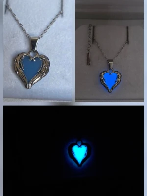 Självlysande halsband, hjärthänge med vingar  - Unikt handgjort halsband med ett hjärtformat hänge i silverfärgad metall och blått självlysande inlägg. Hänget är ca 1,8 cm och har detaljer som liknar vingar runt hjärtat. Kedjan är tunn och silverfärgad i rostfritt stål med justerbar längd. Perfekt för dig som gillar smycken som sticker ut och lyser i mörkret. Effekten aktiveras av vanligt dagsljus och solljus o lyser vanligtvis i flera timmar (12h+) vid normal användning. Tål vatten & missfärgas ej.