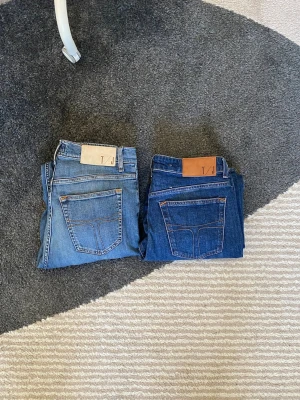 Blå jeans från tiger of sweden 31/32 - Säljer två par klassiska blå jeans från tiger of sweden  i storlek 31/32. Ena paret är ljusblått och det andra mörkblått, båda med kontrastsömmar och läderpatch bak. Tillverkade i Italien och har raka ben. Perfekta för en avslappnad och stilren look.