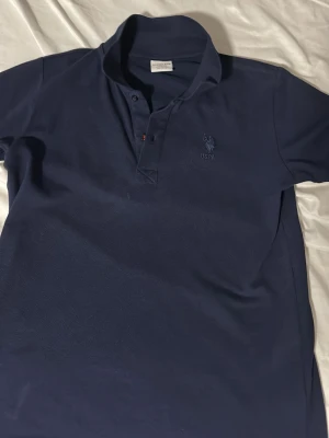 Skjorta från U.S. Polo Assn - Snygg mörkblå henley från U.S. Polo Assn med klassisk krage och diskret logga broderad på bröstet. Skjortan är tillverkad i mjuk bomull och har knappar vid halsen för en avslappnad look. Storlek 146-152cm 11-12years , Mycket bra skick!!!++