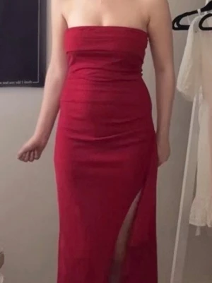 Röd axelbandslös långklänning - Snygg röd axelbandslös långklänning med slits på sidan. Klänningen har en draperad effekt och sitter tight över kroppen. Perfekt för dig som vill ha en elegant och stilren look.