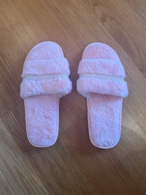 Rosa fluffiga tofflor med strass - fluffiga rosa tofflor med öppen tå och bred rem. Står strl 42-43 men då dom är gjorda i china upplevs dom mer som 40-41! Säljs pga för små. Helt oanvända. 