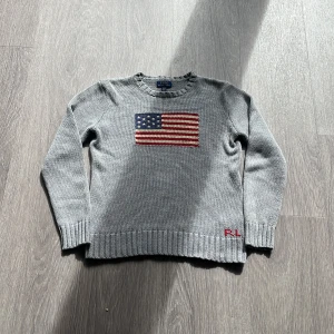 Grå stickad USA tröja Polo Ralph Lauren🇺🇸✨ - Grå stickad tröja från Polo Ralph Lauren med amerikansk flagga broderad på bröstet och RL-broderi vid nederkanten. Tröjan har rund hals, ribbade muddar och lång ärm. Storleken är 18-20 xl men passar bäst xs och sRiktigt stilig och priset är inte bestämt🙌 hör av er