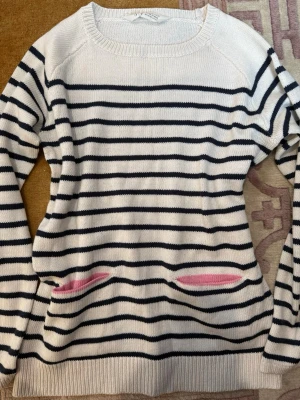 Randig stickad tröja från H&M -  vit stickad tröja från H&M med svarta horisontella ränder och två fickor med rosa detaljer. 