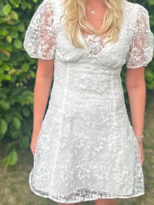 Studentklänning  - Säljer min studentklänning. Den är köpt från secondhand och sedan omsydd hos skräddare, så den är helt unik! Den har puffärmar, v-ringad hals, blommig spets och transparenta ärmar. Har en liten fläck högt upp på ryggen (se sista bilden), kan gå att få bort har inte testat.