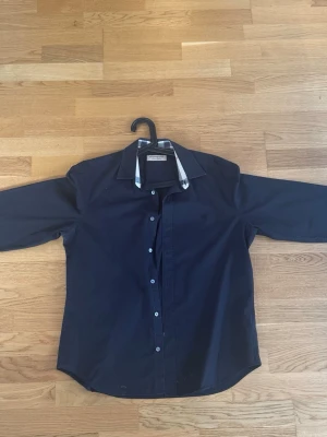 Svart burberry skjorta i mycket gott skick - En svart burberry skjorta i storlek L. Har inga fläckar, hål eller andra fel. Mycket gott skick!