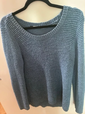 Blå stickad tröja med vid hals - Säljer en blå stickad tröja med avslappnad passform och bred, rundad halsringning som kan bäras off-shoulder. Tröjan har långa ärmar och är stickad i ett mjukt, luftigt material. Perfekt för en chill och trendig look.