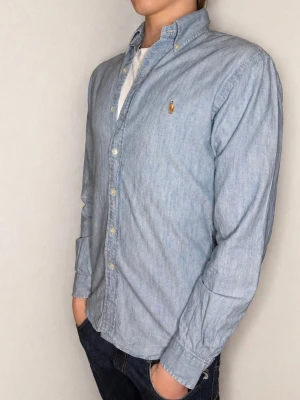 Ralph Lauren jeansskjorta - Säljer en väldigt fet denim skjorta från Ralph Lauren i färgen ljusblå.  Skjortan är i mycket fint skick och är perfekt nu till våren och sommaren! Passformen är slim fit. Nypris är ca 1800, men jag säljer för endast 299. Kontakta mig för frågor eller prisförslag!!